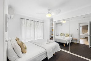 Une chambre d’hôtel moderne équipée d’un grand miroir, d’un lit, d’une armoire et d’un ventilateur de plafond.