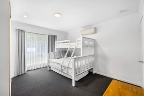 Ein Zimmer mit Etagenbett, einem Vorhangfenster, einem Heizkörper und einer Deckenleuchte.