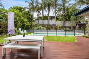 Une terrasse avec une table et des chaises blanches, une piscine et une plateforme en bois.