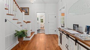 Un pasillo con una escalera de madera, un candelabro, una recepción y una puerta que da a otra habitación.