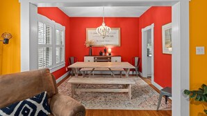 Un comedor con mesa y sillas de madera, una lámpara de araña y una pared roja decorativa.
