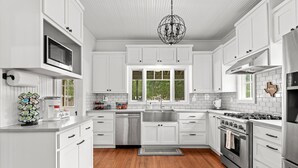 Una cocina moderna con armarios blancos, electrodomésticos de acero inoxidable, un ventanal grande y una lámpara de araña.