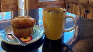 Interior de una cabaña de madera con una mesa que tiene un muffin, una taza y un tenedor sobre un plato.