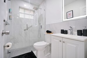 Un baño moderno con ducha envuelta en vidrio, inodoro blanco y tocador con espejo.