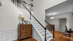 A staircase with white railings and dark balusters, a wooden dresser with drawers, a lamp, and a desk with a chair. - Stunning 5 bedroom/3 bath home in Hope Valley Farm (Durham)