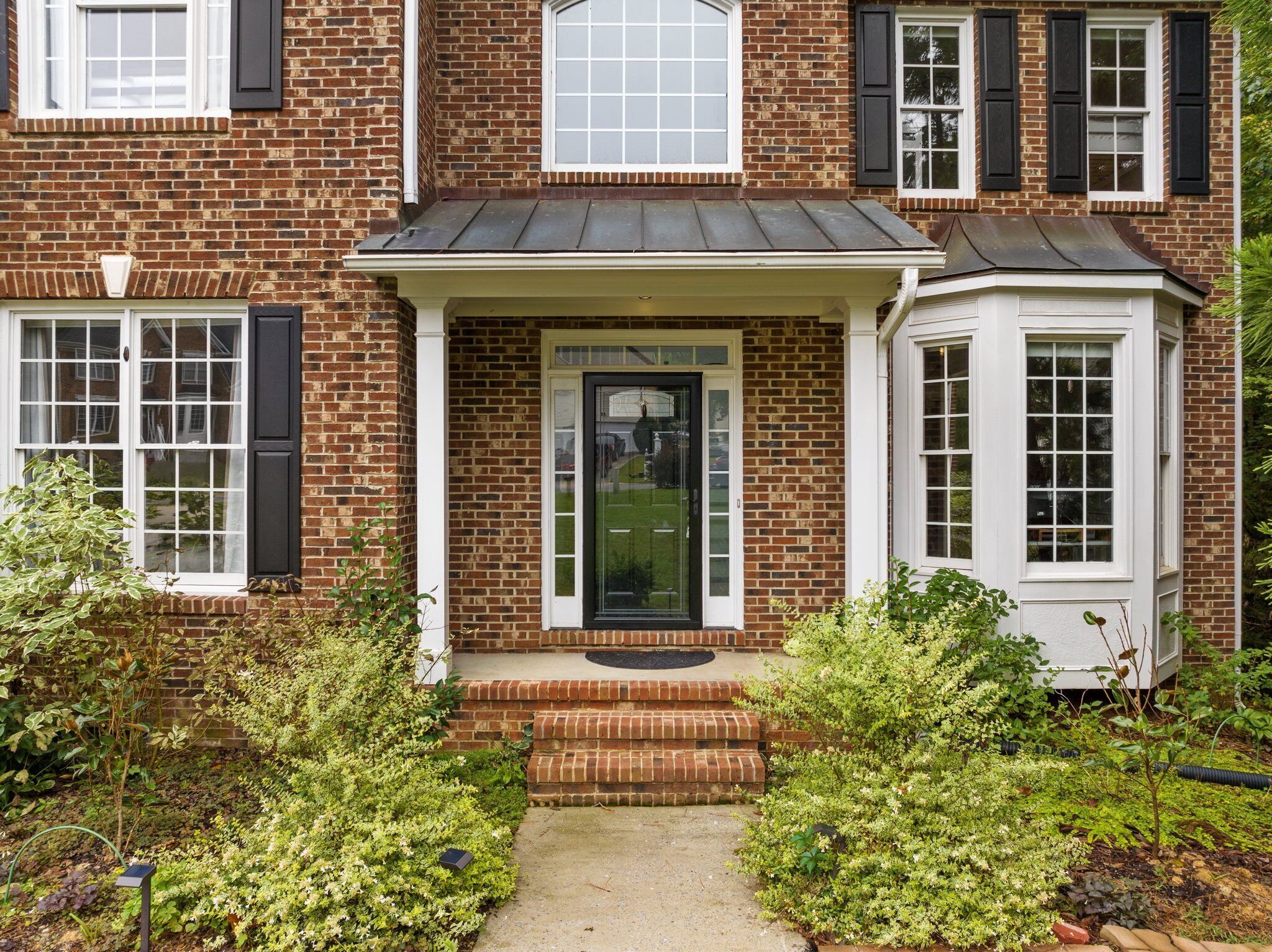 A two-story brick house with a front porch, a bay window, and a small attached garage.