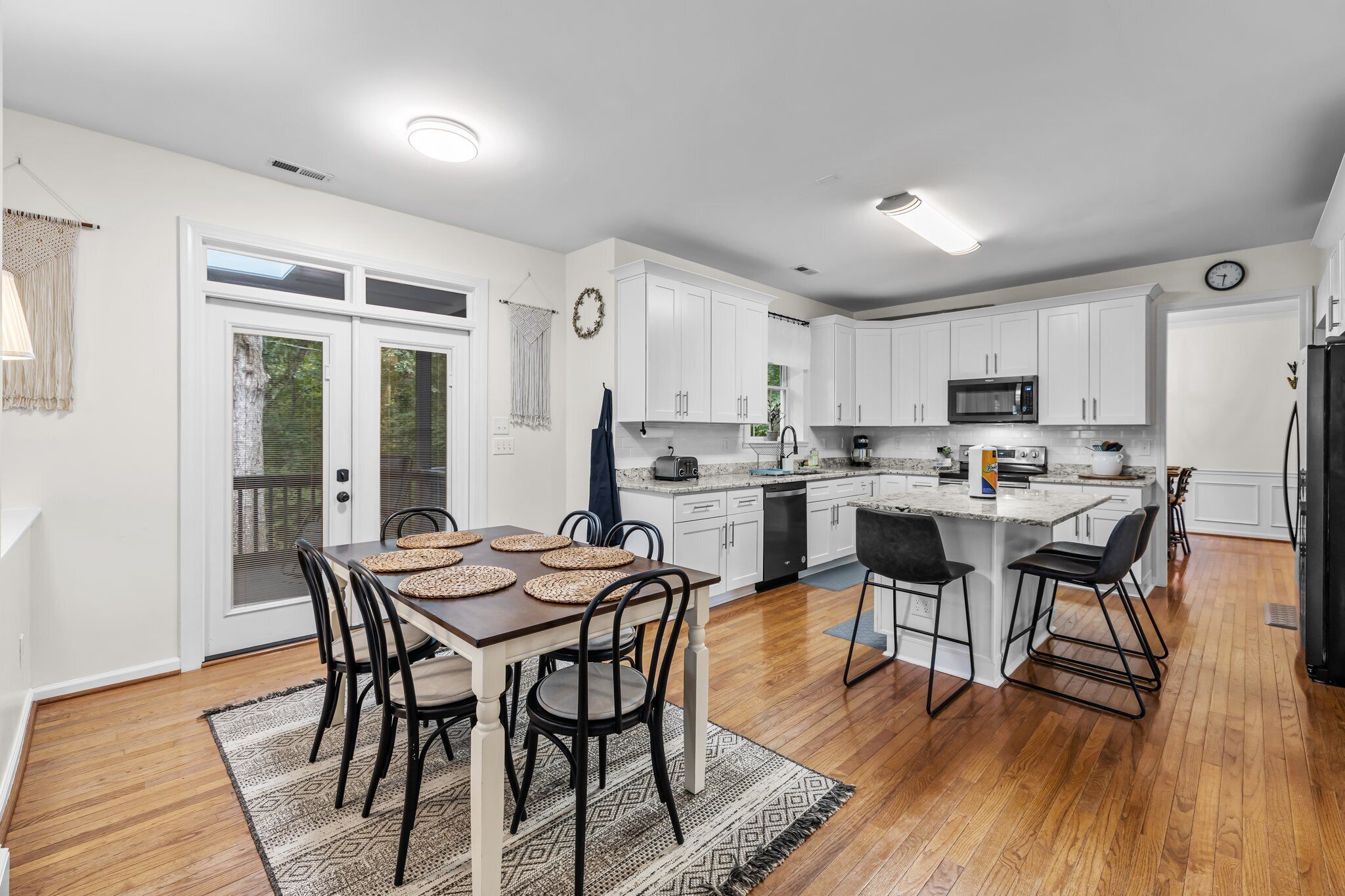 A modern kitchen with white cabinets, a central island, and a dining area with a wooden table and chairs.
