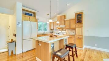 Une cuisine moderne avec des meubles en bois, un réfrigérateur blanc, un îlot central doté de tabourets et un éclairage suspendu.