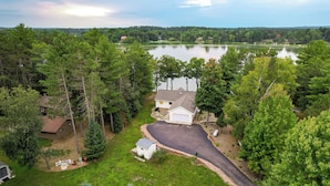 A residential area with a house, driveway, and a lake in the background. - Spacious Lakefront New Auburn Home w/ Sunroom (New Auburn)