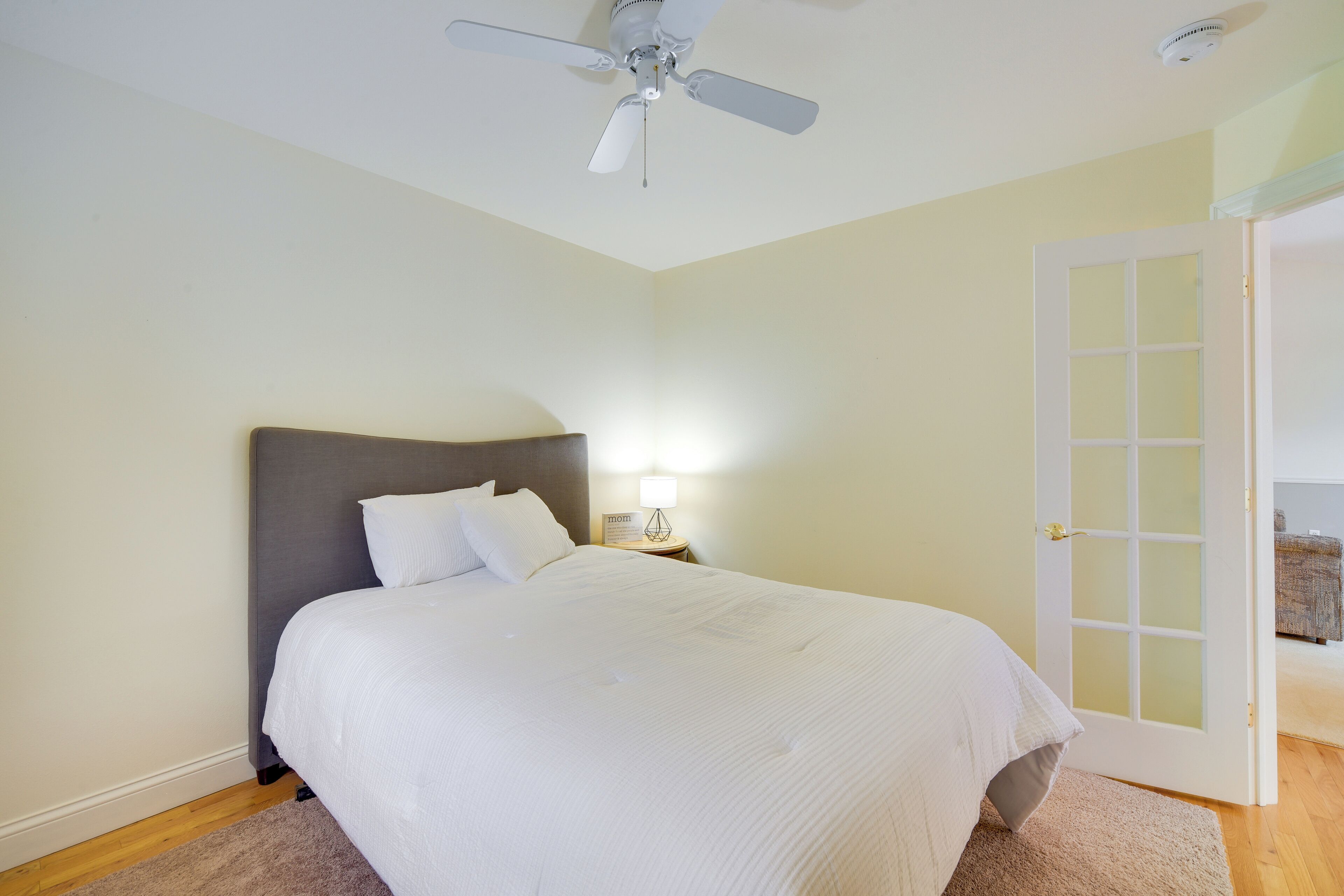 A bedroom with a bed, a nightstand, a lamp, a ceiling fan, and a door to another room.