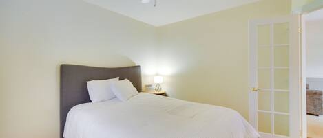 A bedroom with a bed, a nightstand, a lamp, a ceiling fan, and a door to another room.