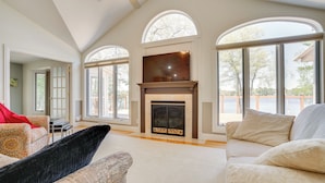 A spacious living room with a fireplace, large windows, and a high ceiling. - Spacious Lakefront New Auburn Home w/ Sunroom (New Auburn)
