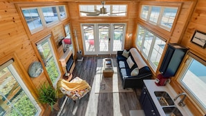 A cozy cabin with a wooden interior, large windows, a ceiling fan, a sofa, a coffee table, and a kitchen area. - Outdoor Pool & Patio: Quiet Whitney Retreat! (Whitney)