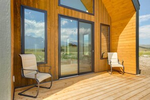 Una cabaña de madera con grandes puertas correderas de vidrio, dos sillas en una terraza y vista a las montañas.