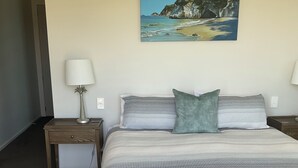 Un dormitorio con una cama, dos mesitas de noche, una lámpara y un cuadro de una playa.
