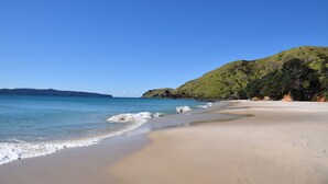 Una playa con agua azul cristalina, orilla de arena y colinas verdes al fondo.