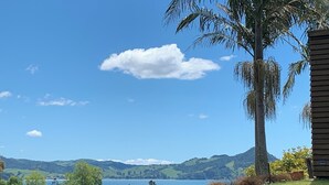 Un paisaje costero con cielo despejado, una palmera grande y vista de un lago y colinas al fondo.