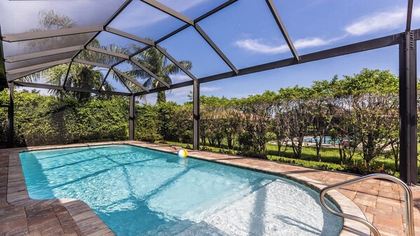 A covered outdoor swimming pool with a view of a landscaped garden and distant buildings.