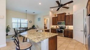 A modern kitchen with granite countertops, stainless steel appliances, wooden cabinets, and a ceiling fan.