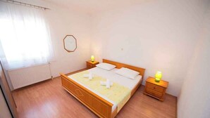 A single-bed room with a wooden frame, two bedside tables with lamps, a radiator, and a window with curtains. - Holiday flat with a beautiful view (Okrug Gornji)