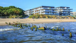 Un hotel sulla spiaggia con numerosi balconi, una spiaggia sabbiosa e una costa rocciosa con alghe.