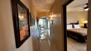 A hotel hallway with framed artwork on the walls, a polished floor, and a view into a bedroom with a bed and nightstand. - Scott Beach Villa #3 (St Thomas)