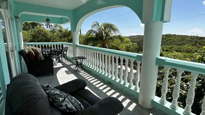 A covered outdoor seating area with a white balustrade, wicker furniture, and a view of a lush landscape. - Scott Beach Villa #3 (St Thomas)