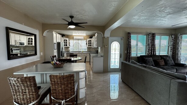 A spacious living area with a grey sofa, a dining table with chairs, and a kitchen in the background. - Scott Beach Villa #3 (St Thomas)