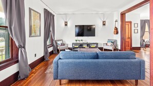 Un salon avec un canapé bleu, un plancher en bois, un téléviseur à écran plat et une guitare.