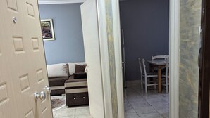 Una habitación con una cama, una mesita y una silla. Se ve una puerta que da a otra habitación.