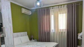 Un dormitorio con cama, mesita de noche, lámpara, silla y ventana con cortinas.
