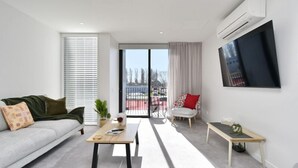 Een moderne woonkamer met een bank, salontafel, tv aan de muur en een balkon met uitzicht op de stad.