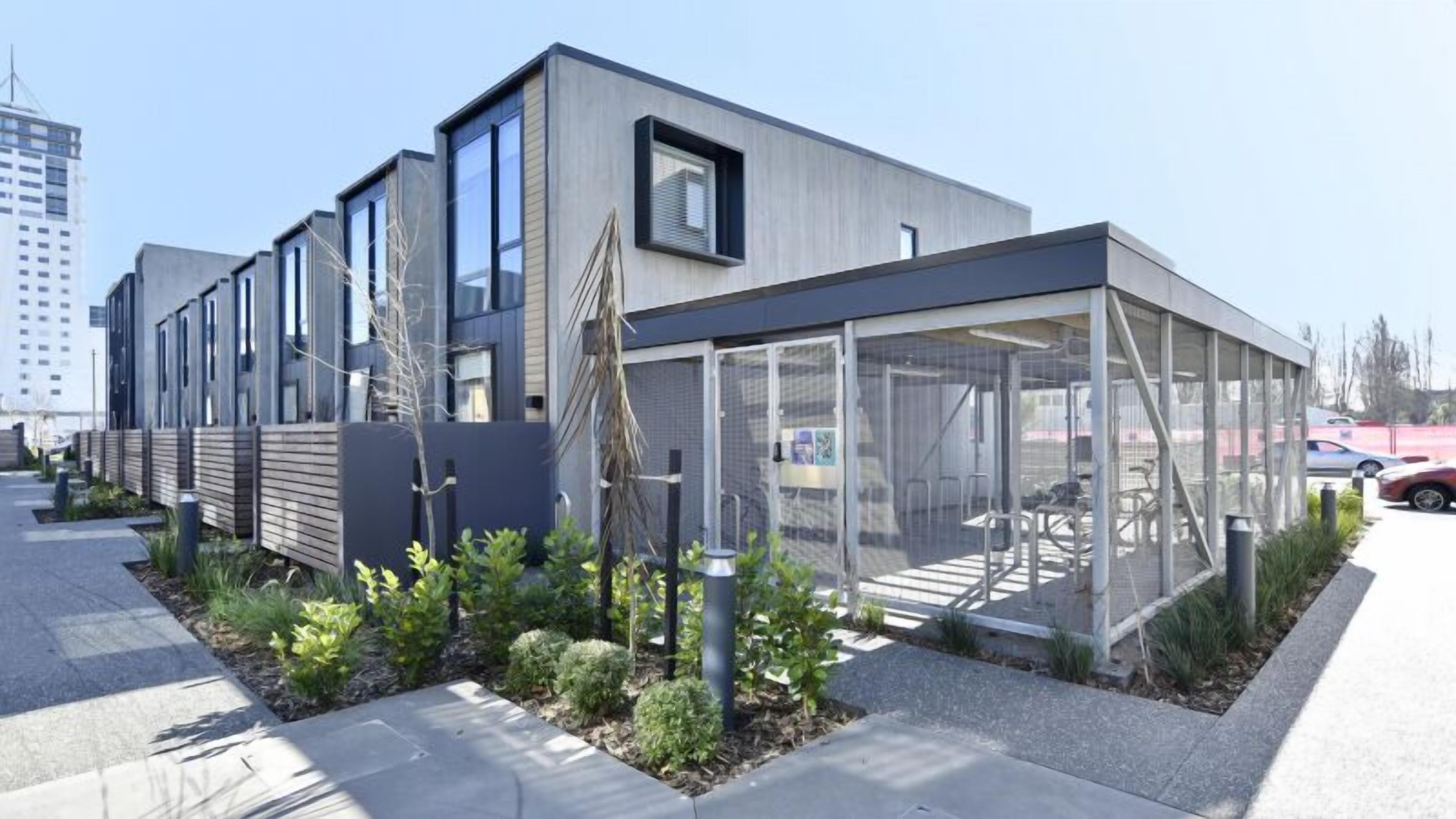 A modern building with a glass enclosure, a covered outdoor area, and a landscaped garden.