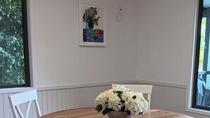 Ein Essbereich mit einem runden Holztisch, weißen Polsterstühlen und einer Vase mit weißen Blumen auf dem Tisch.