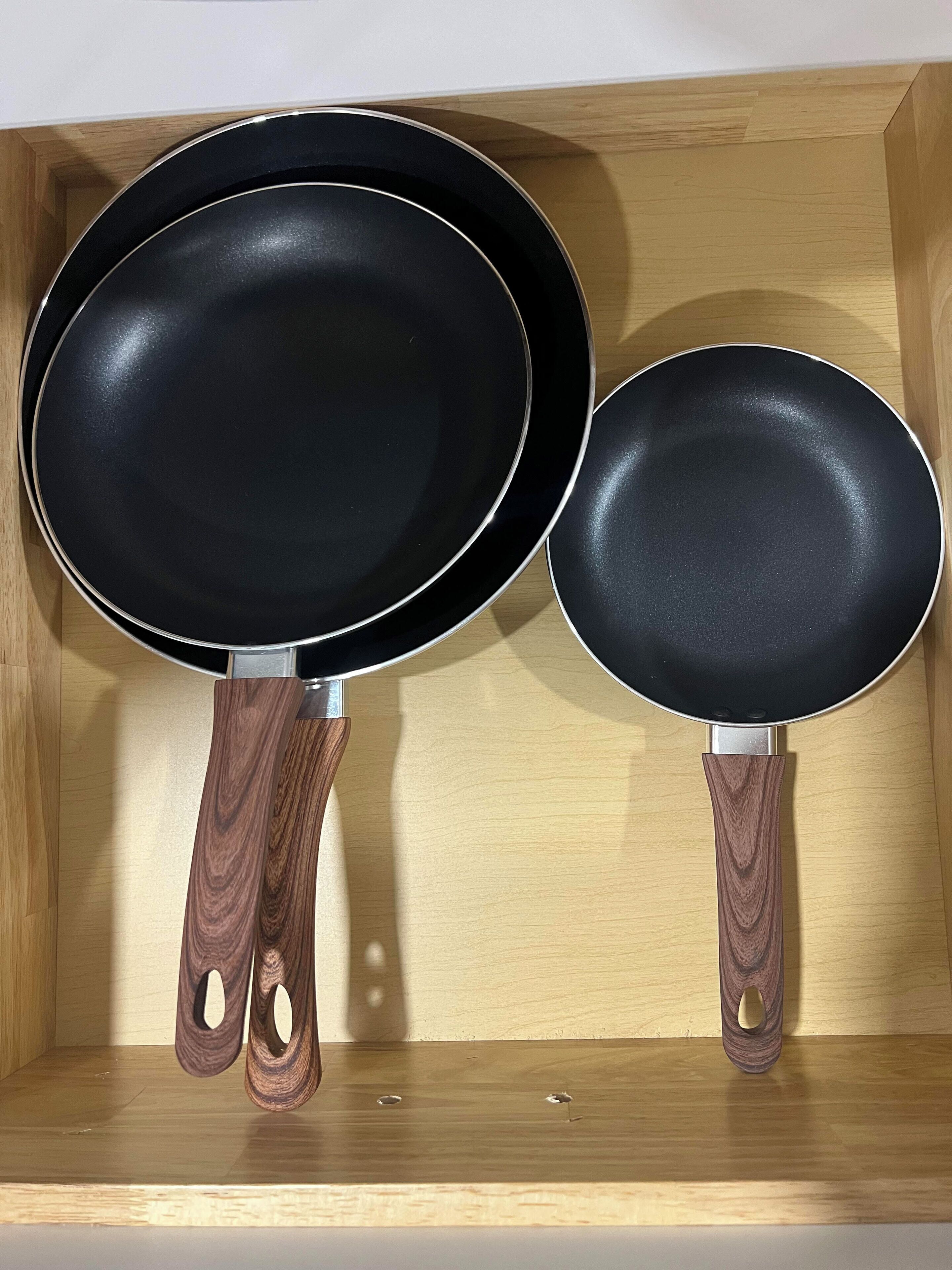 Two black frying pans with wooden handles in a wooden box.