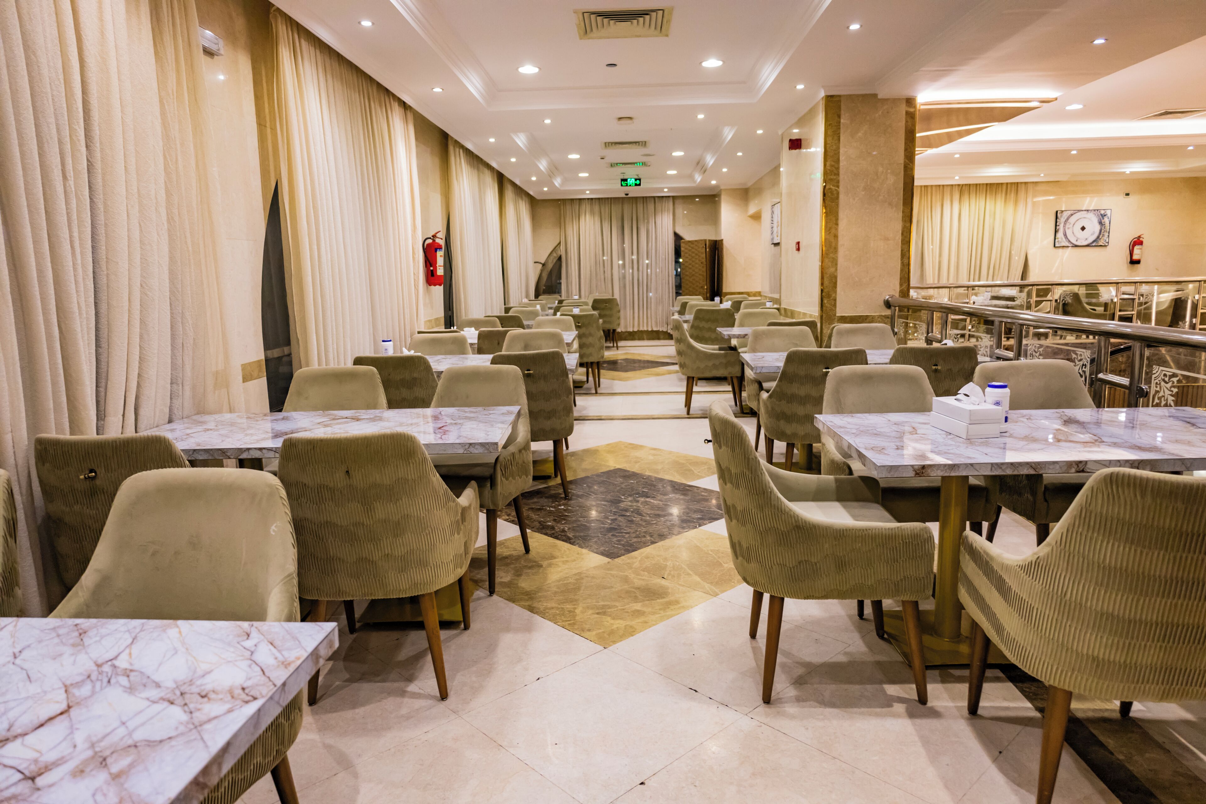 A hotel dining area with marble tables, cushioned chairs, and a patterned carpet.
