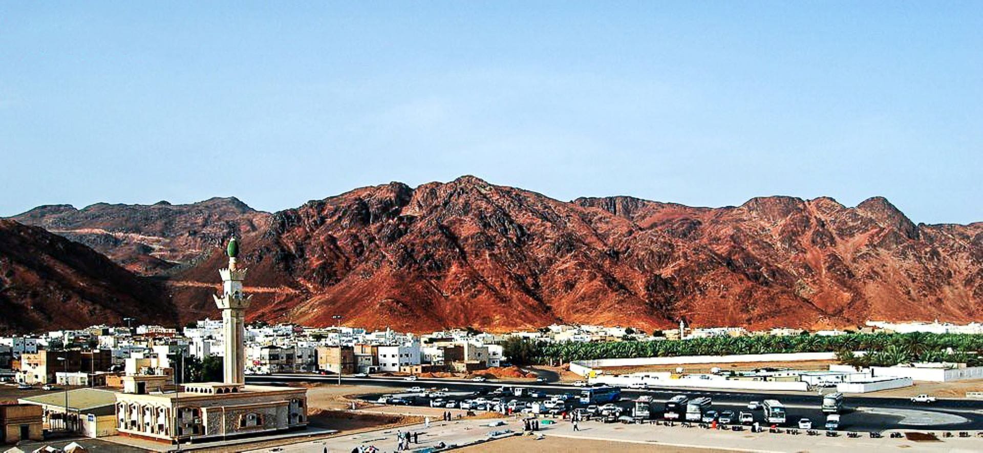 Un pueblo con un minarete destacado, una autopista y montañas al fondo.