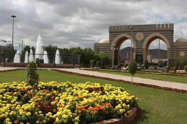A landscaped area with a fountain, a large archway, and a flower bed with yellow flowers.