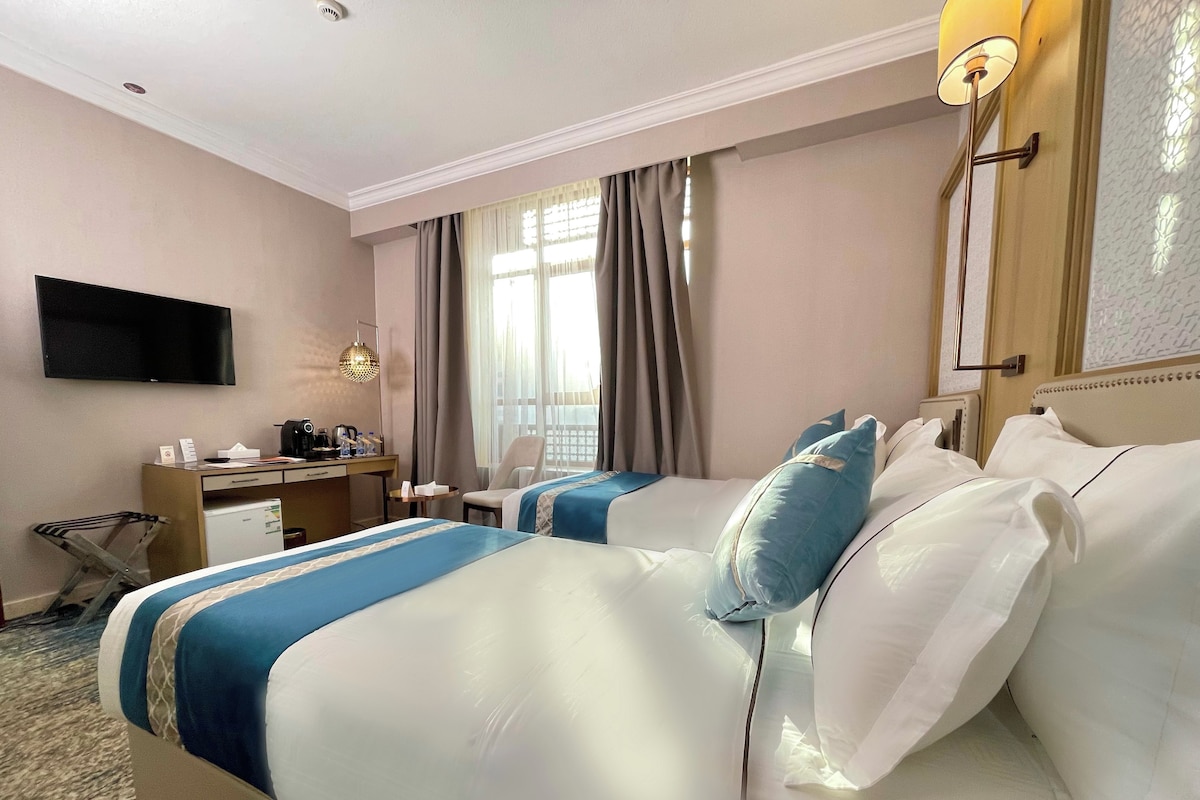 Une chambre d’hôtel avec deux lits, un bureau, une chaise, une télévision et une fenêtre avec des rideaux.
