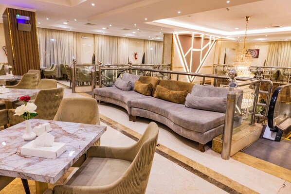 Un hall d’hôtel moderne avec un comptoir d’accueil en marbre, des fauteuils confortables, un escalier et un lustre.