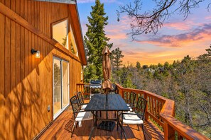 A wooden deck with a table and chairs, a barbecue grill, and a view of trees and a sunset. - Luxury 5BR Hot Tub · Fire Pit · GameRoom Sleep 11 (Big Bear Lake)