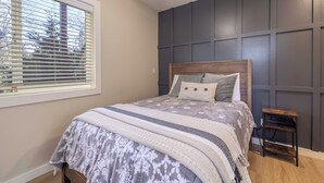 Una camera da letto con un letto, una finestra con persiane, un comodino e un rivestimento murale decorativo.