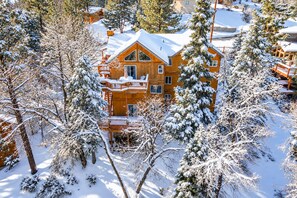 Une cabane en bois à plusieurs étages, dotée d’un balcon et entourée d’arbres couverts de neige.
