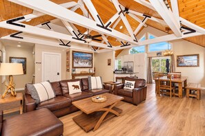 A spacious living room with a large brown leather sectional sofa, a wooden coffee table, and a dining area with a wooden table and chairs.