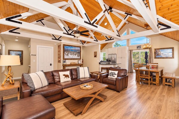 A spacious living room with a large brown leather sectional sofa, a wooden coffee table, and a dining area with a wooden table and chairs. - Luxury 5BR Hot Tub · Fire Pit · GameRoom Sleep 11 (Big Bear Lake)
