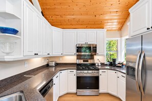 Une cuisine moderne avec des meubles blancs, des appareils en acier inoxydable, des comptoirs en granit et un plafond en bois.