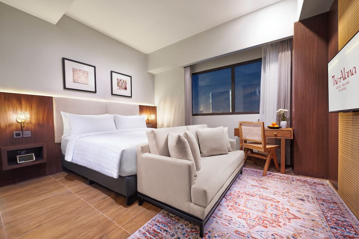A hotel room with a bed, a sofa, a desk, and a large window.