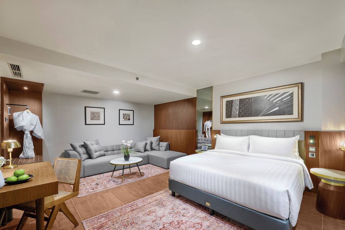 A modern hotel room with a large bed, a sofa, a dining area, and a bathroom.