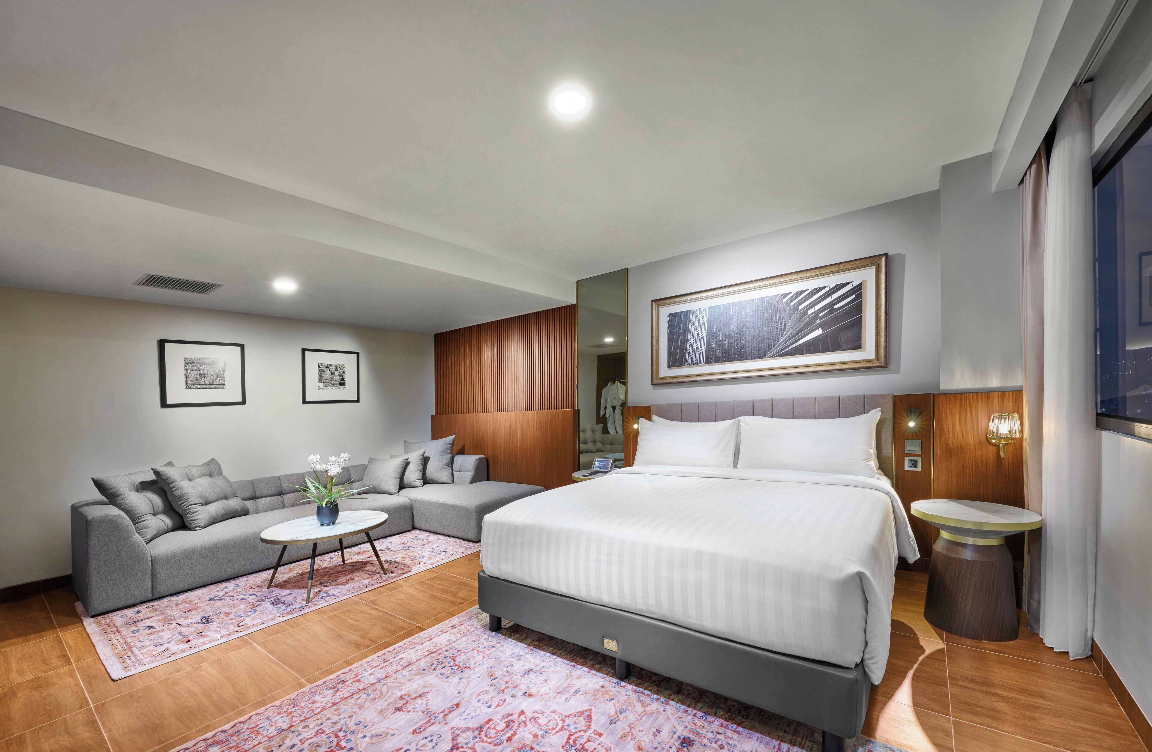 A modern hotel room with a large bed, a sofa, a small table, and a TV.