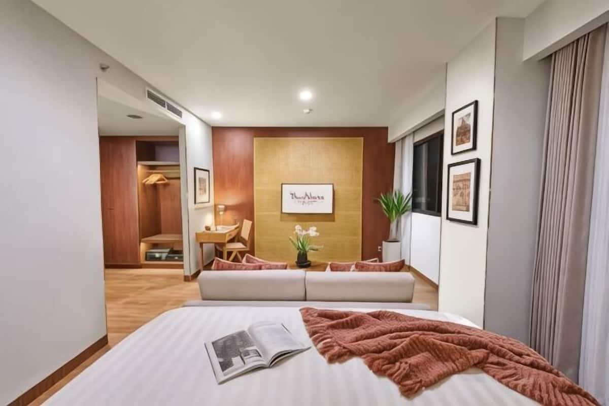 A hotel room with a bed, a reading area with a sofa, a wooden accent wall, and framed pictures.